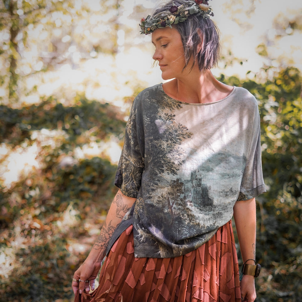 
                  
                    Castles in the Air Luxe Tee featuring Jan Brueghel’s whimsical 1600s landscape and painterly floral trim on soft bamboo-based viscose – Market of Stars.
                  
                