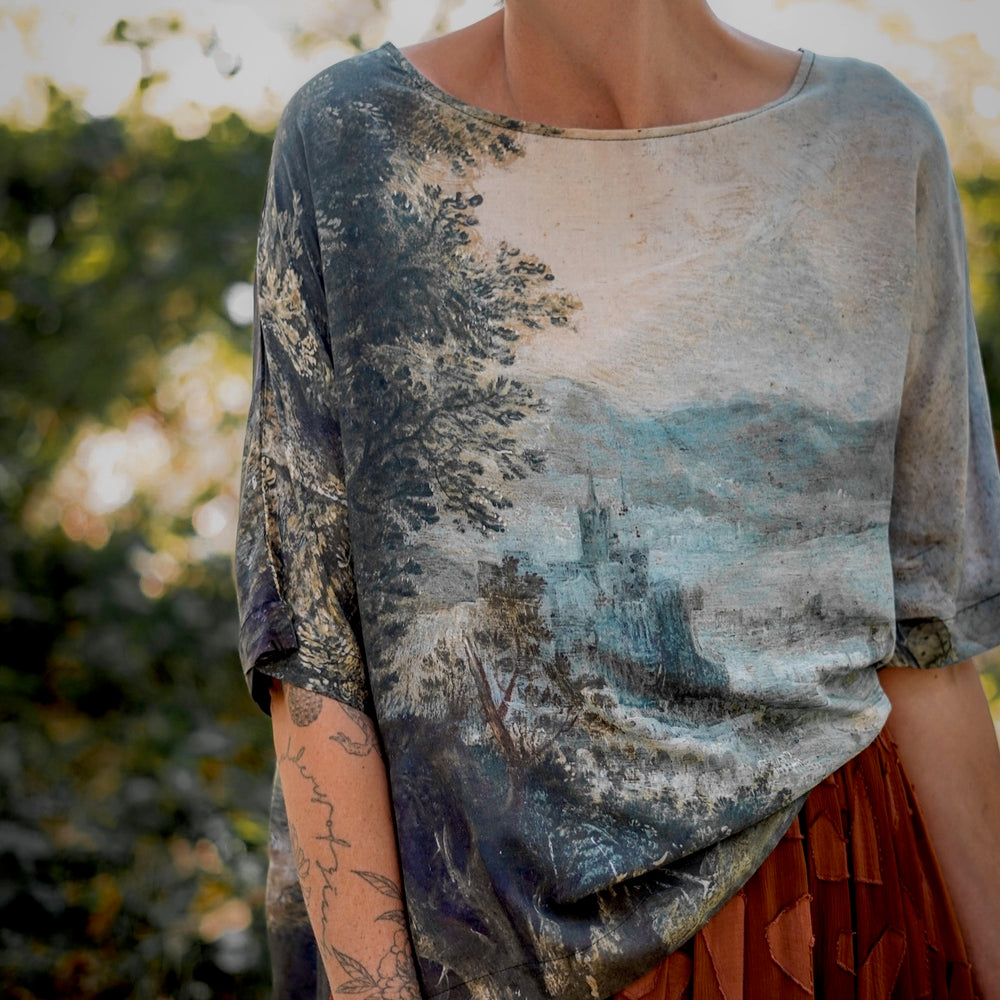 
                  
                    Castles in the Air Luxe Tee featuring Jan Brueghel’s whimsical 1600s landscape and painterly floral trim on soft bamboo-based viscose – Market of Stars.
                  
                