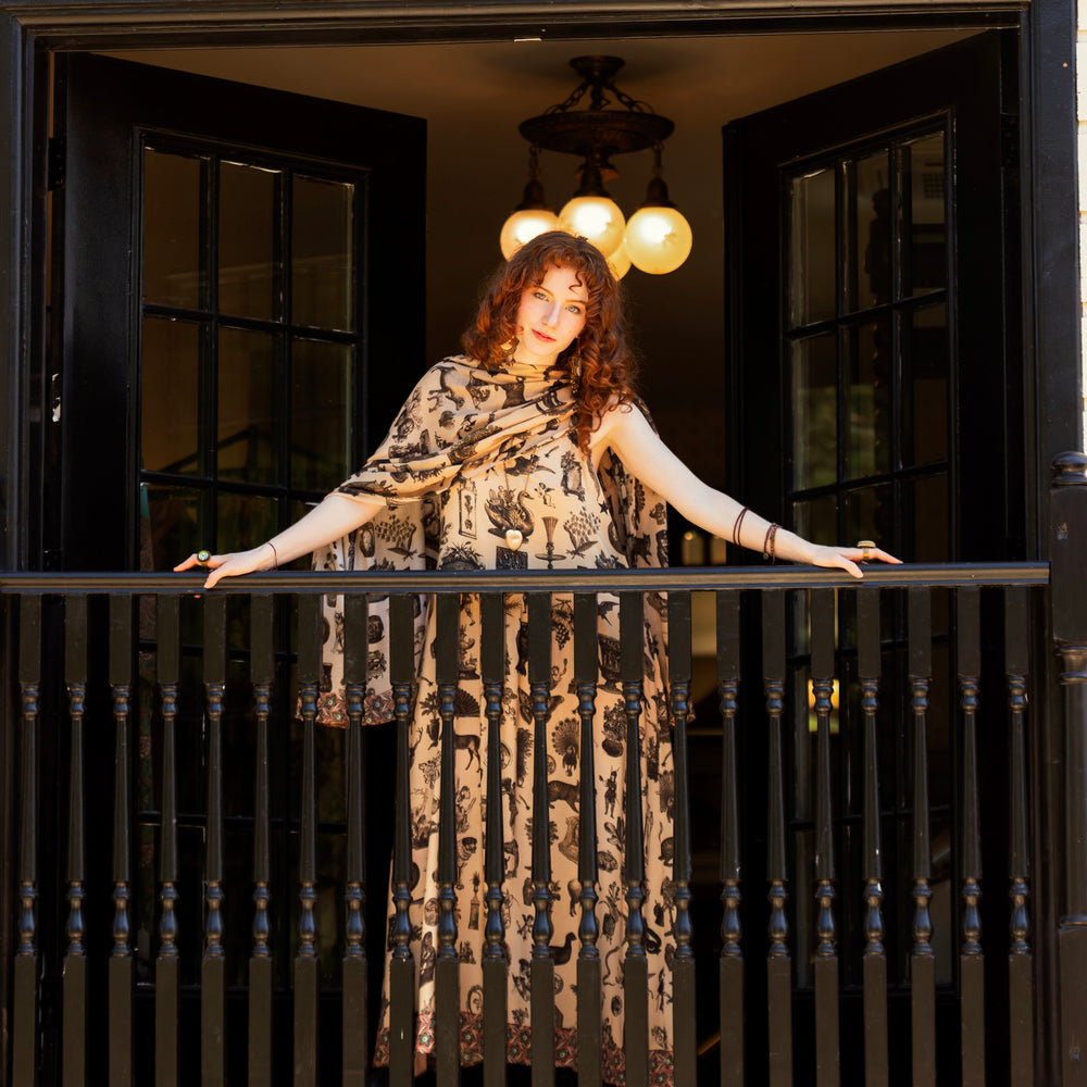 
                  
                    Model wearing a bamboo-viscose scarf inspired by a mysterious Victorian scrapbook. This whimsical print celebrates the wonder hidden in ordinary things — Market of Stars.
                  
                