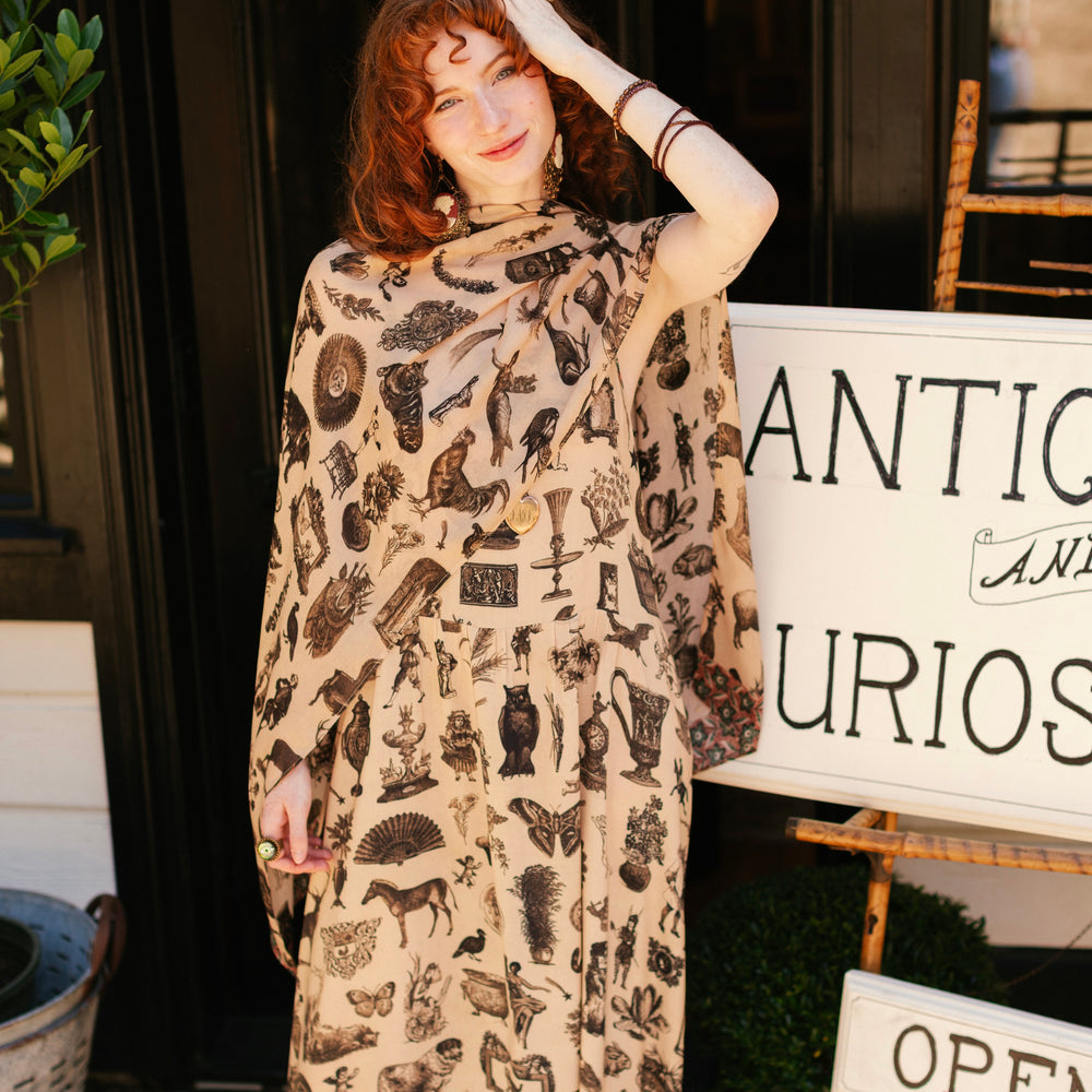 
                  
                    Model wearing a bamboo-viscose scarf inspired by a mysterious Victorian scrapbook. This whimsical print celebrates the wonder hidden in ordinary things — Market of Stars.
                  
                