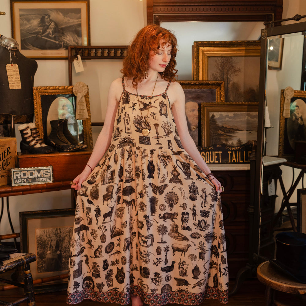Model wearing a maxi-length bamboo viscose slip dress inspired by a mysterious Victorian scrapbook. This whimsical print celebrates the wonder hidden in ordinary things — Market of Stars.