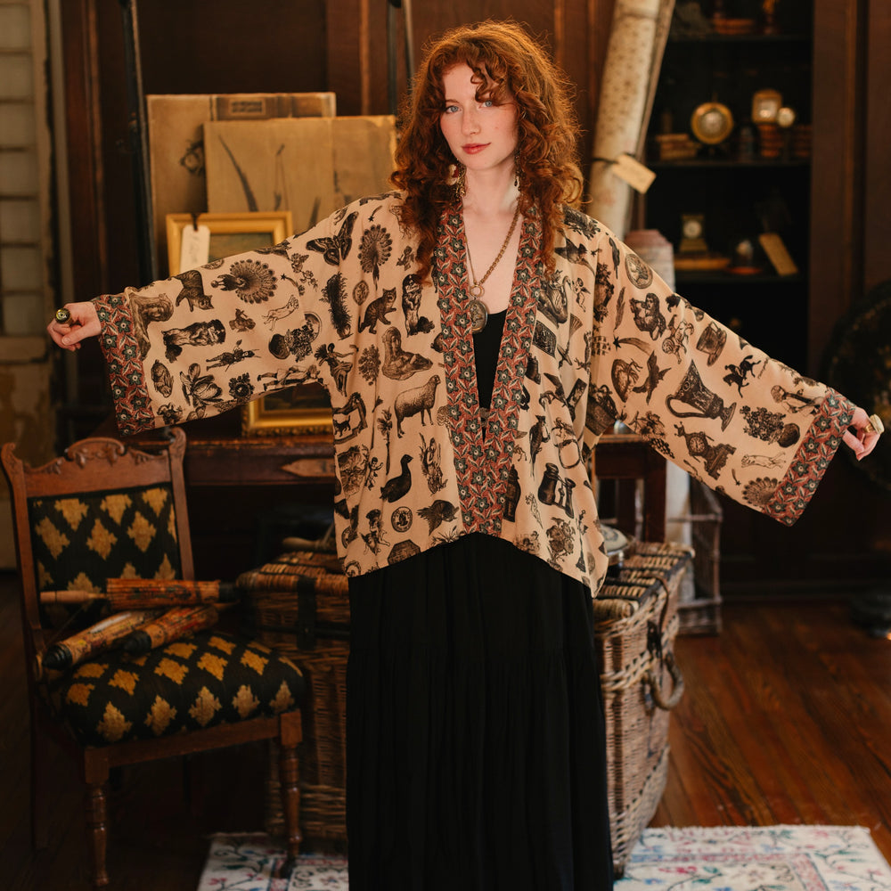 
                  
                    Model wearing a bamboo-viscose cropped length duster inspired by a mysterious Victorian scrapbook. This whimsical print celebrates the wonder hidden in ordinary things — Market of Stars.
                  
                