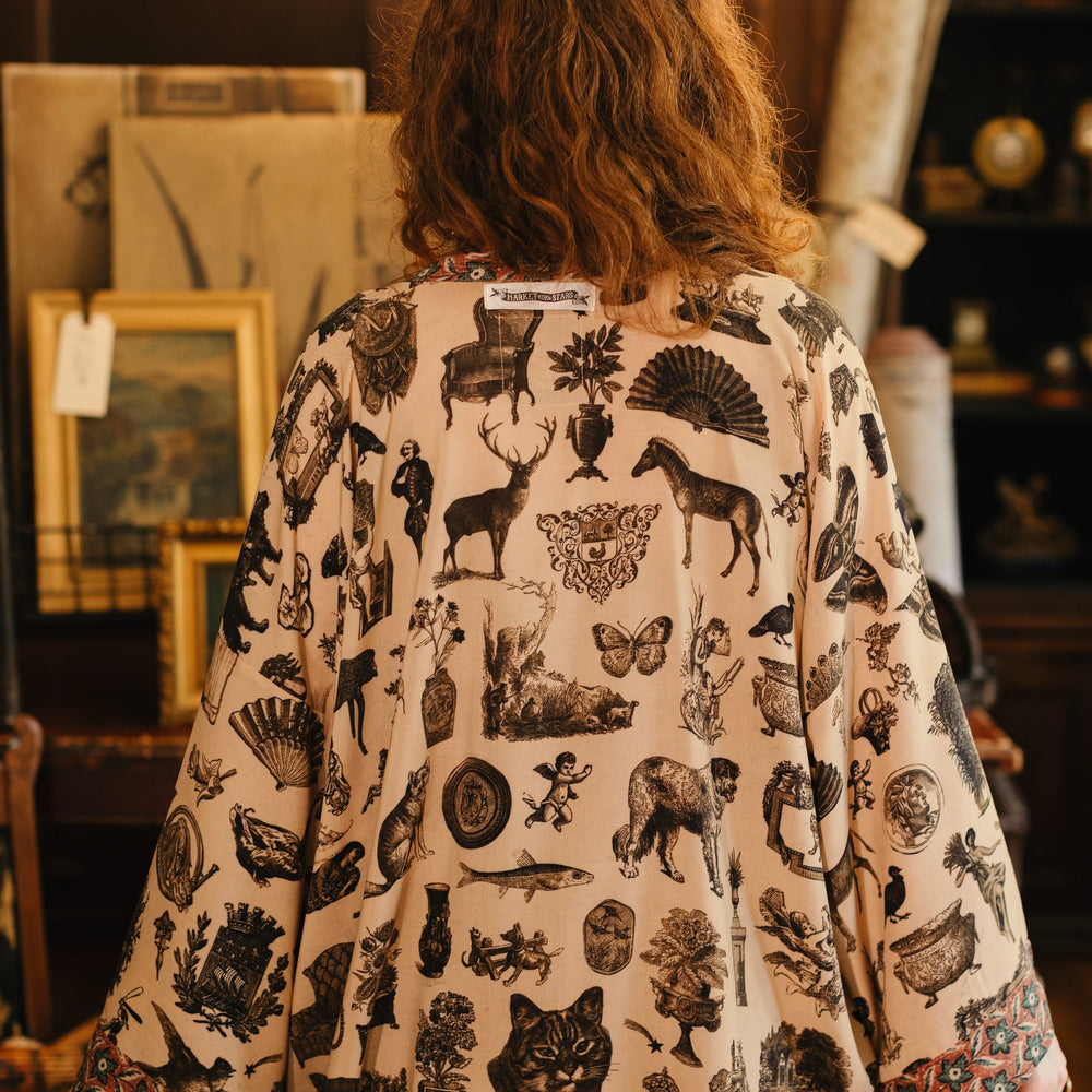 
                  
                    Model wearing a bamboo-viscose cropped length duster inspired by a mysterious Victorian scrapbook. This whimsical print celebrates the wonder hidden in ordinary things — Market of Stars.
                  
                