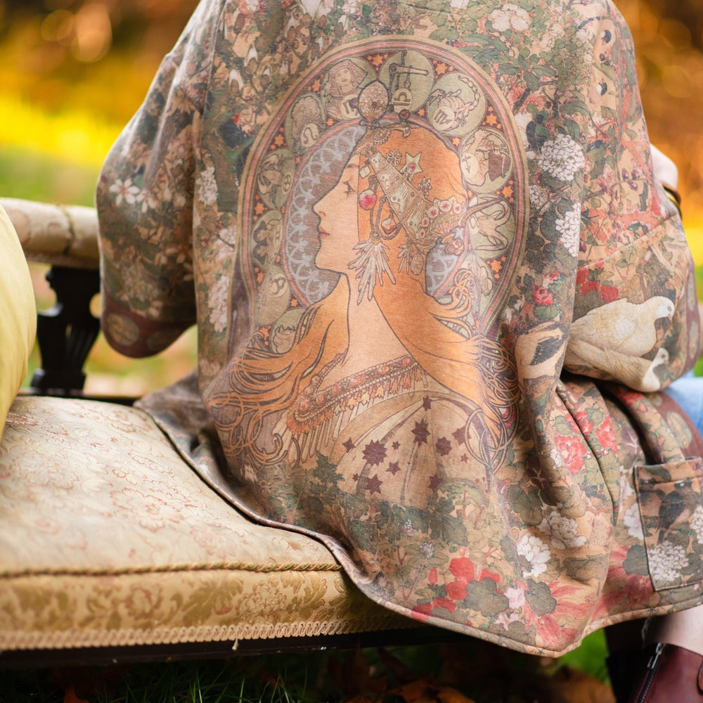 
                  
                    Model wearing Dreamweaver Cottage Cardigan featuring Mucha’s 1896 zodiac woman with celestial crown, printed on cozy fleece-lined cotton blend – Market of Stars
                  
                