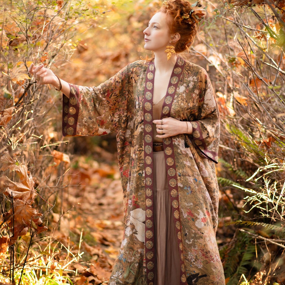 
                  
                    Model wearing Dreamweaver Opera Duster – featuring Alphonse Mucha’s zodiac woman, celestial crown, and burgundy zodiac trim inspired by 1970s luxe bohemian style – Market of Stars.
                  
                