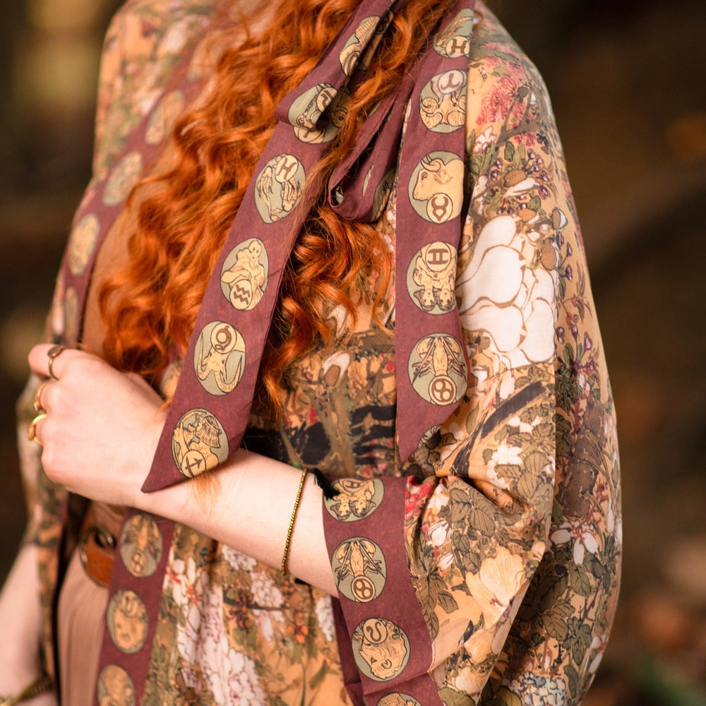 
                  
                    Model wearing Dreamweaver Opera Duster – featuring Alphonse Mucha’s zodiac woman, celestial crown, and burgundy zodiac trim inspired by 1970s luxe bohemian style – Market of Stars.
                  
                