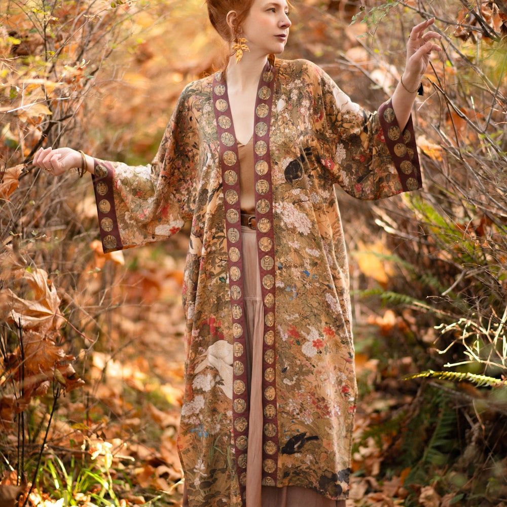 
                  
                    Model wearing Dreamweaver Opera Duster – featuring Alphonse Mucha’s zodiac woman, celestial crown, and burgundy zodiac trim inspired by 1970s luxe bohemian style – Market of Stars.
                  
                