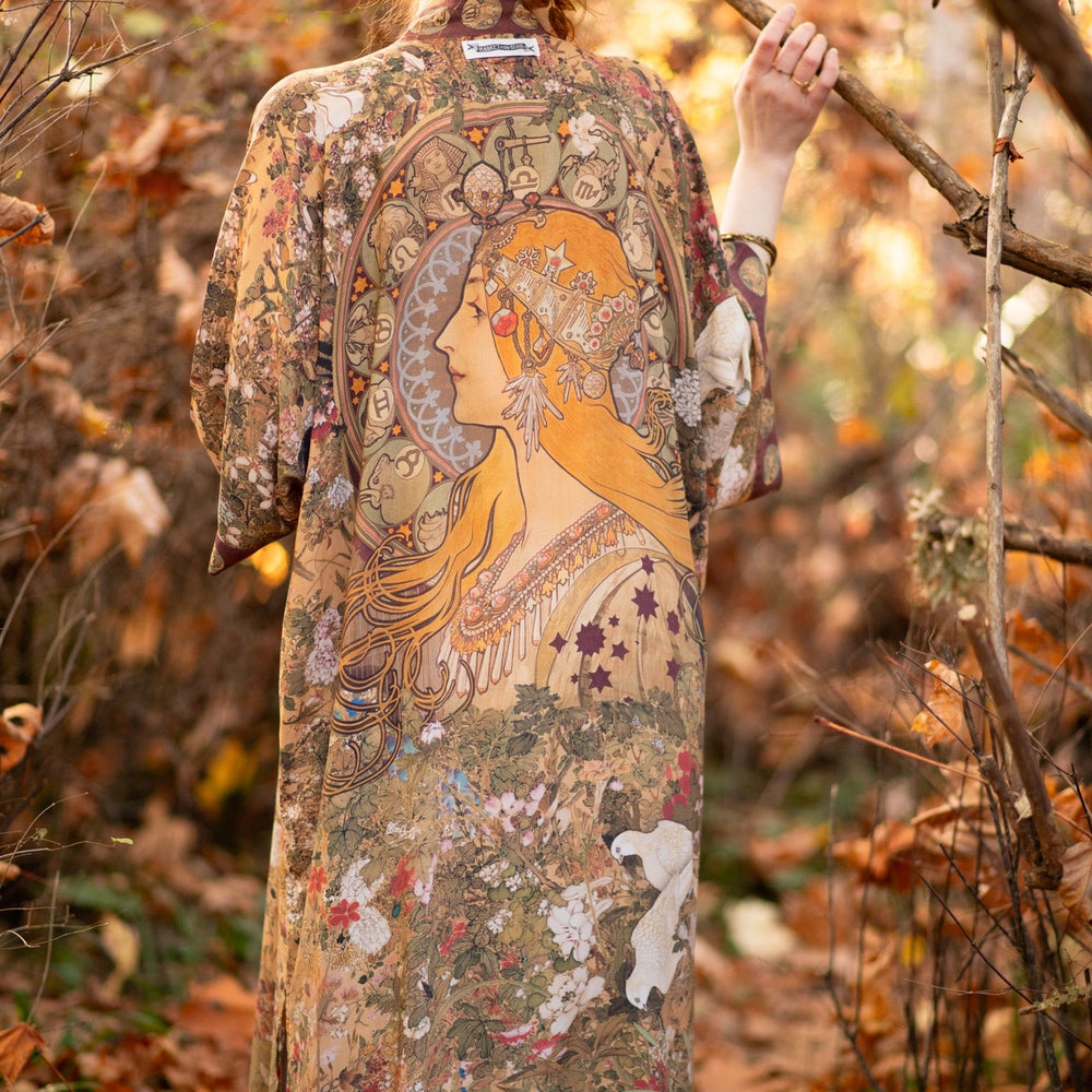 
                  
                    Model wearing Dreamweaver Opera Duster – featuring Alphonse Mucha’s zodiac woman, celestial crown, and burgundy zodiac trim inspired by 1970s luxe bohemian style – Market of Stars.
                  
                