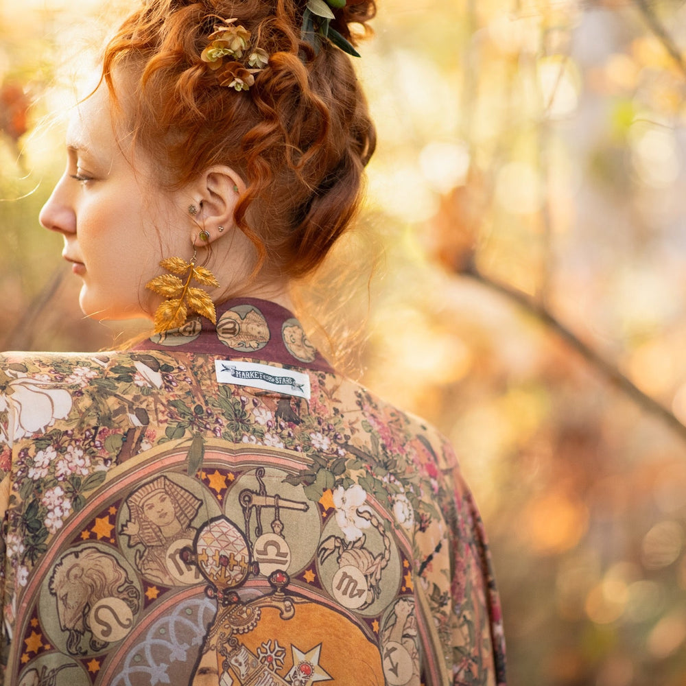 
                  
                    Model wearing Dreamweaver Opera Duster – featuring Alphonse Mucha’s zodiac woman, celestial crown, and burgundy zodiac trim inspired by 1970s luxe bohemian style – Market of Stars.
                  
                