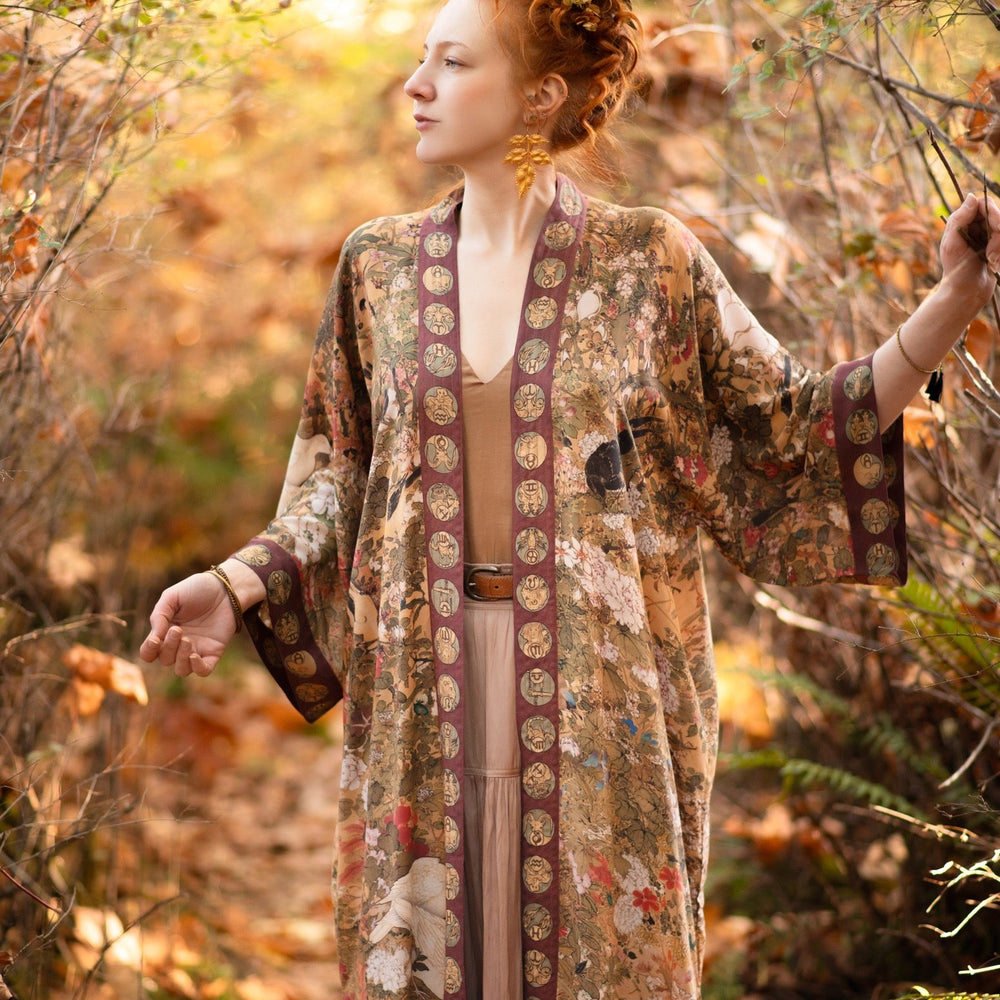 
                  
                    Model wearing Dreamweaver Opera Duster – featuring Alphonse Mucha’s zodiac woman, celestial crown, and burgundy zodiac trim inspired by 1970s luxe bohemian style – Market of Stars.
                  
                