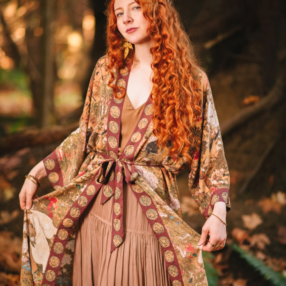 
                  
                    Model wearing Dreamweaver Opera Duster – featuring Alphonse Mucha’s zodiac woman, celestial crown, and burgundy zodiac trim inspired by 1970s luxe bohemian style – Market of Stars.
                  
                