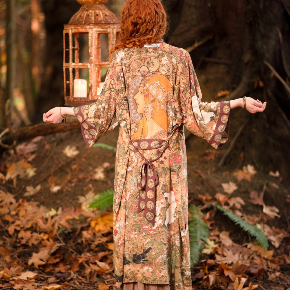 
                  
                    Model wearing Dreamweaver Opera Duster – featuring Alphonse Mucha’s zodiac woman, celestial crown, and burgundy zodiac trim inspired by 1970s luxe bohemian style – Market of Stars.
                  
                