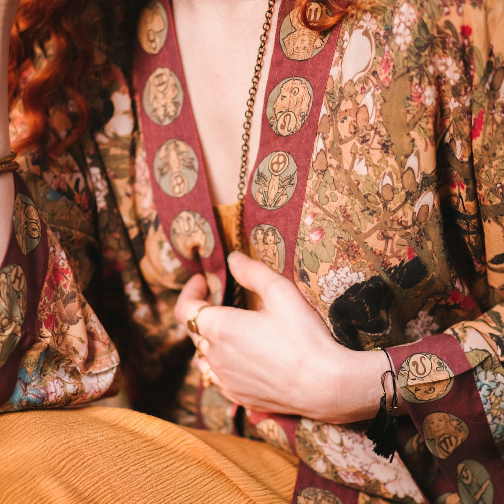 
                  
                    Model wearing Dreamweaver Matinée Duster featuring Alphonse Mucha’s 1896 zodiac woman – trimmed with celestial symbols on deep burgundy background – Market of Stars.
                  
                
