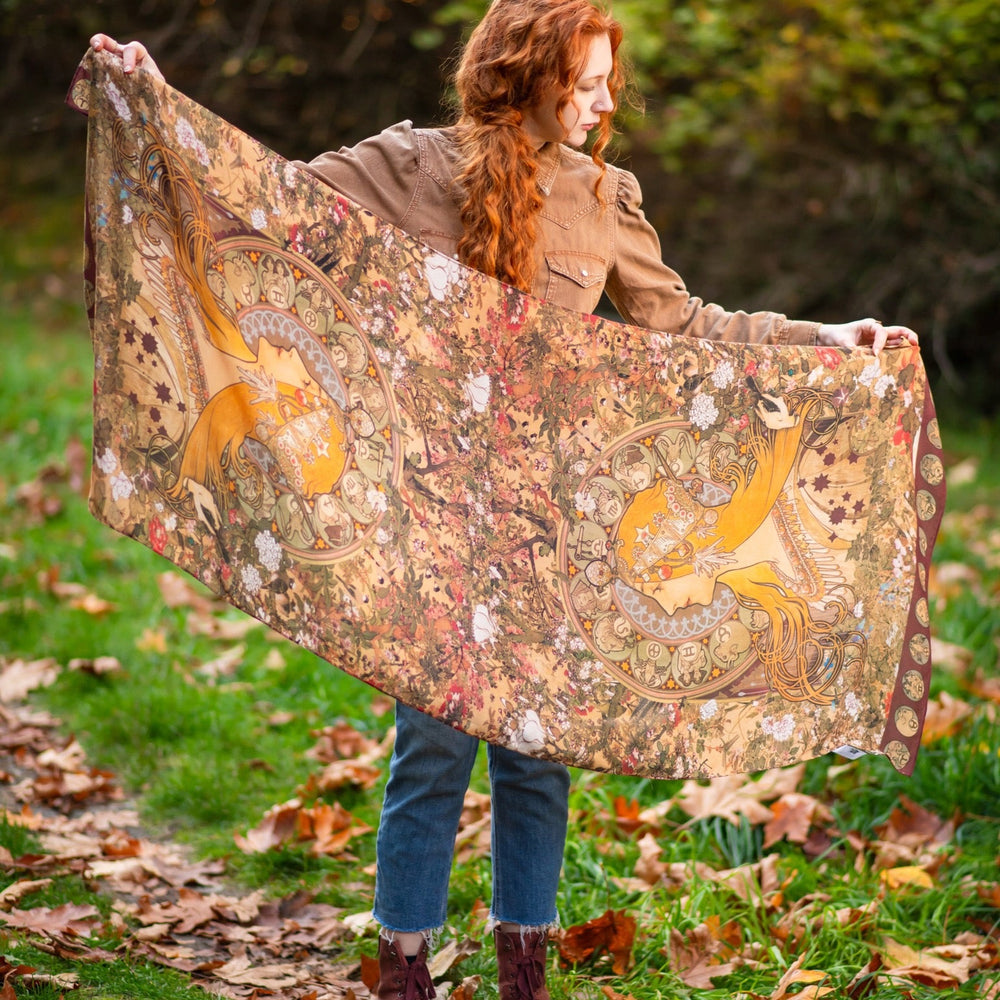 
                  
                    Model wearing Dreamweaver Zodiac Scarf – featuring Alphonse Mucha’s 1896 celestial woman surrounded by zodiac signs and floral scroll artwork – Market of Stars.
                  
                