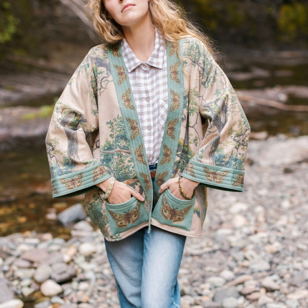 
                  
                    Model wearing Earth and Sky Cottage Jacket – featuring Charles Aston’s tree painting and antique moth art – cozy fleece-lined cardigan for cooler days – Market of Stars.
                  
                