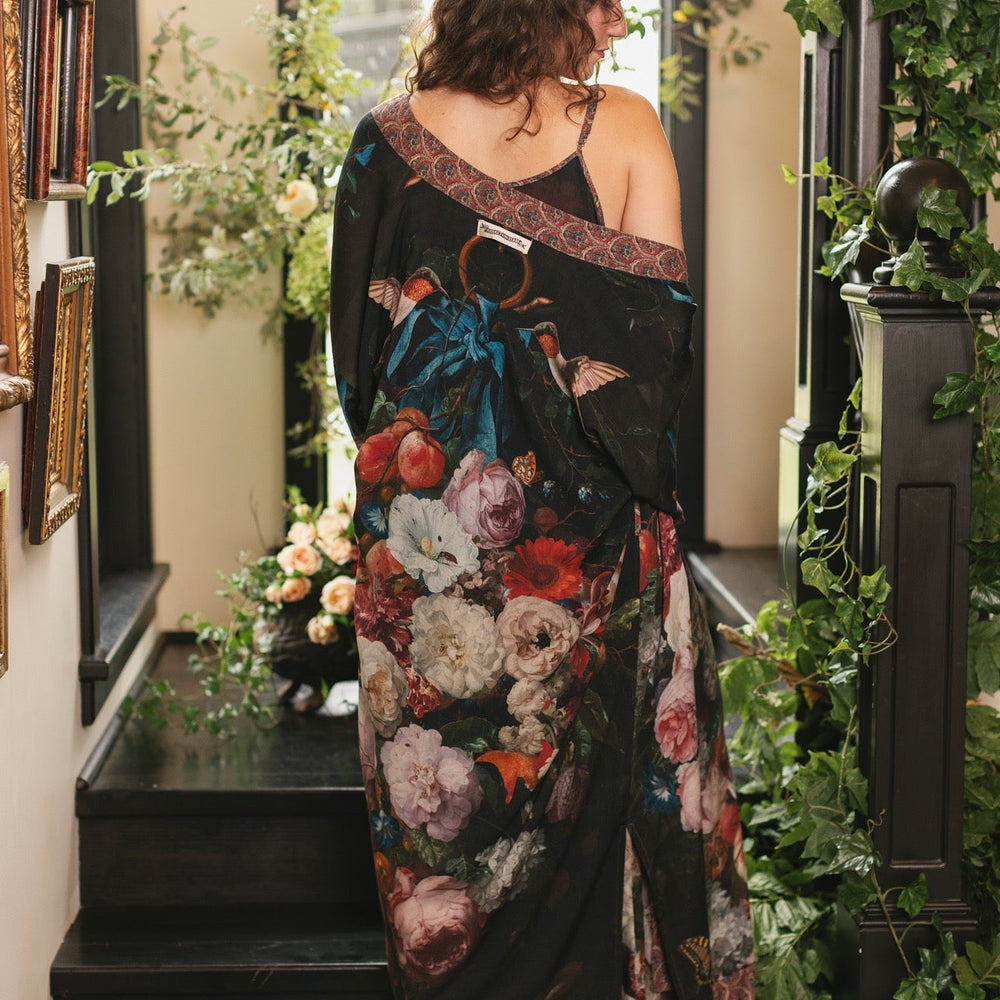 
                  
                    Model showcasing the Flight of Fancy Opera Robe featuring vibrant hummingbirds and historic floral paintings by Rachel Ruysch – Market of Stars.
                  
                
