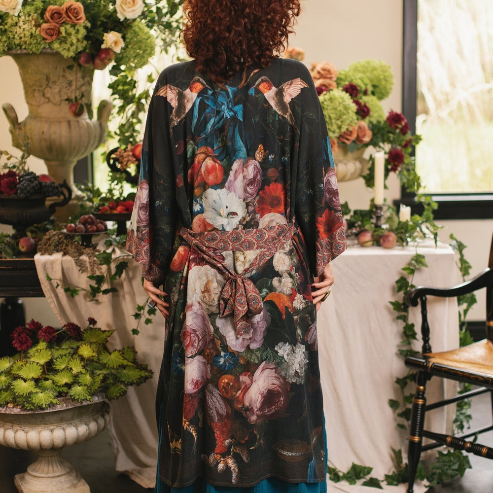 
                  
                    Model showcasing the Flight of Fancy Opera Robe featuring vibrant hummingbirds and historic floral paintings by Rachel Ruysch – Market of Stars.
                  
                