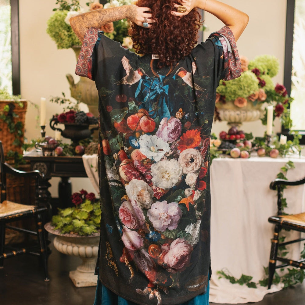
                  
                    Model showcasing the Flight of Fancy Opera Robe featuring vibrant hummingbirds and historic floral paintings by Rachel Ruysch – Market of Stars.
                  
                