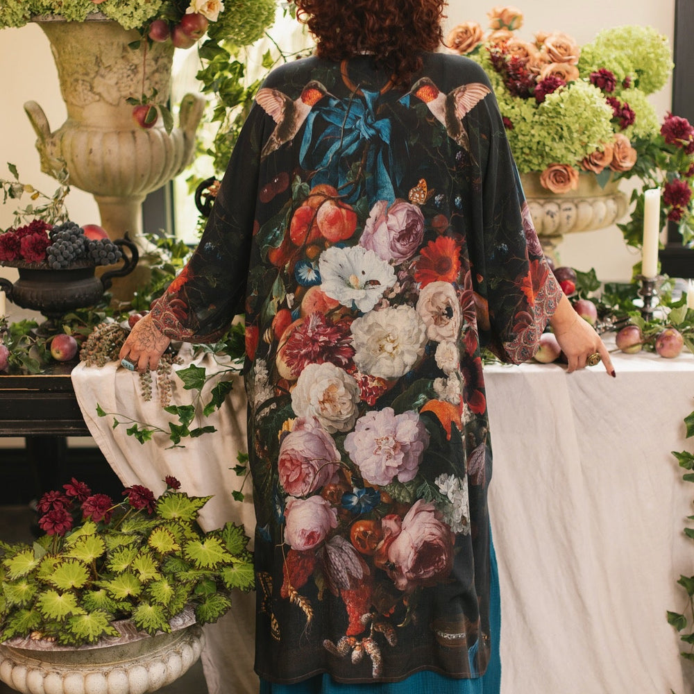 
                  
                    Model showcasing the Flight of Fancy Opera Robe featuring vibrant hummingbirds and historic floral paintings by Rachel Ruysch – Market of Stars.
                  
                