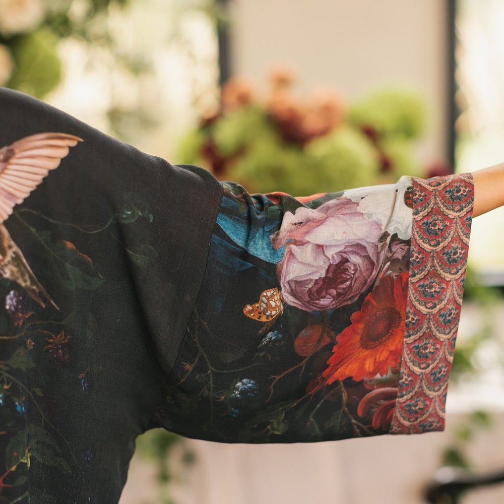 
                  
                    Model showcasing the Flight of Fancy Opera Robe featuring vibrant hummingbirds and historic floral paintings by Rachel Ruysch – Market of Stars.
                  
                