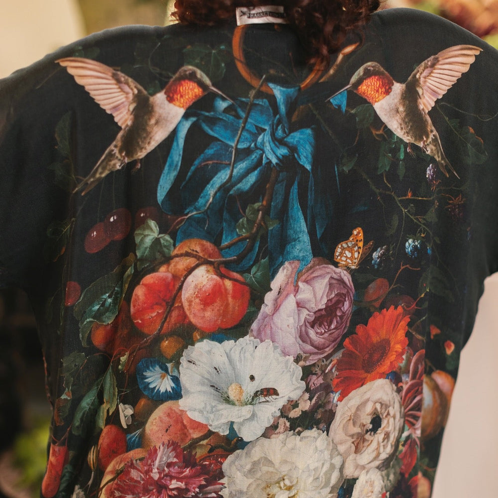 
                  
                    Model showcasing the Flight of Fancy Opera Robe featuring vibrant hummingbirds and historic floral paintings by Rachel Ruysch – Market of Stars.
                  
                