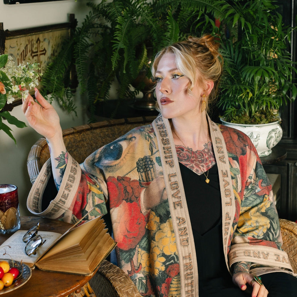 
                  
                    Model wearing cozy printed cardigan with vintage symbols of love, truth, and friendship, featuring charming wood-grain trim and patch pockets – Market of Stars.
                  
                