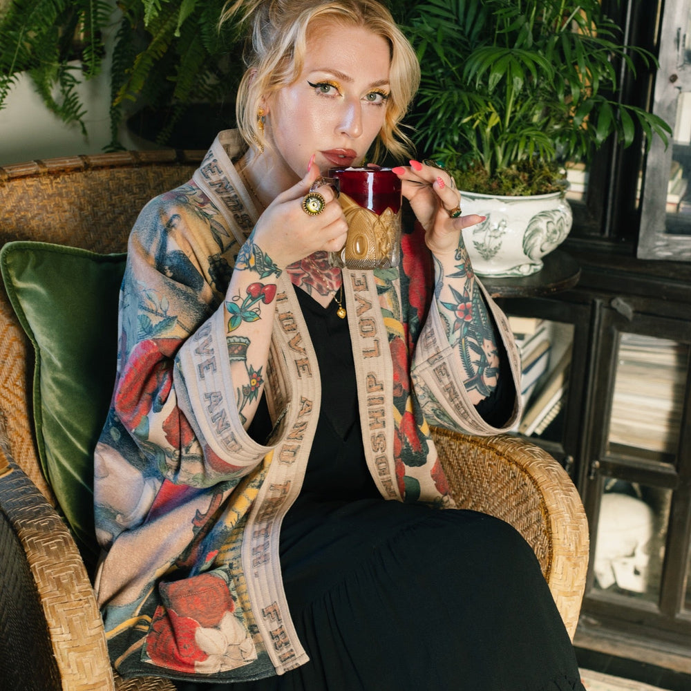 
                  
                    Model wearing cozy printed cardigan with vintage symbols of love, truth, and friendship, featuring charming wood-grain trim and patch pockets – Market of Stars.
                  
                