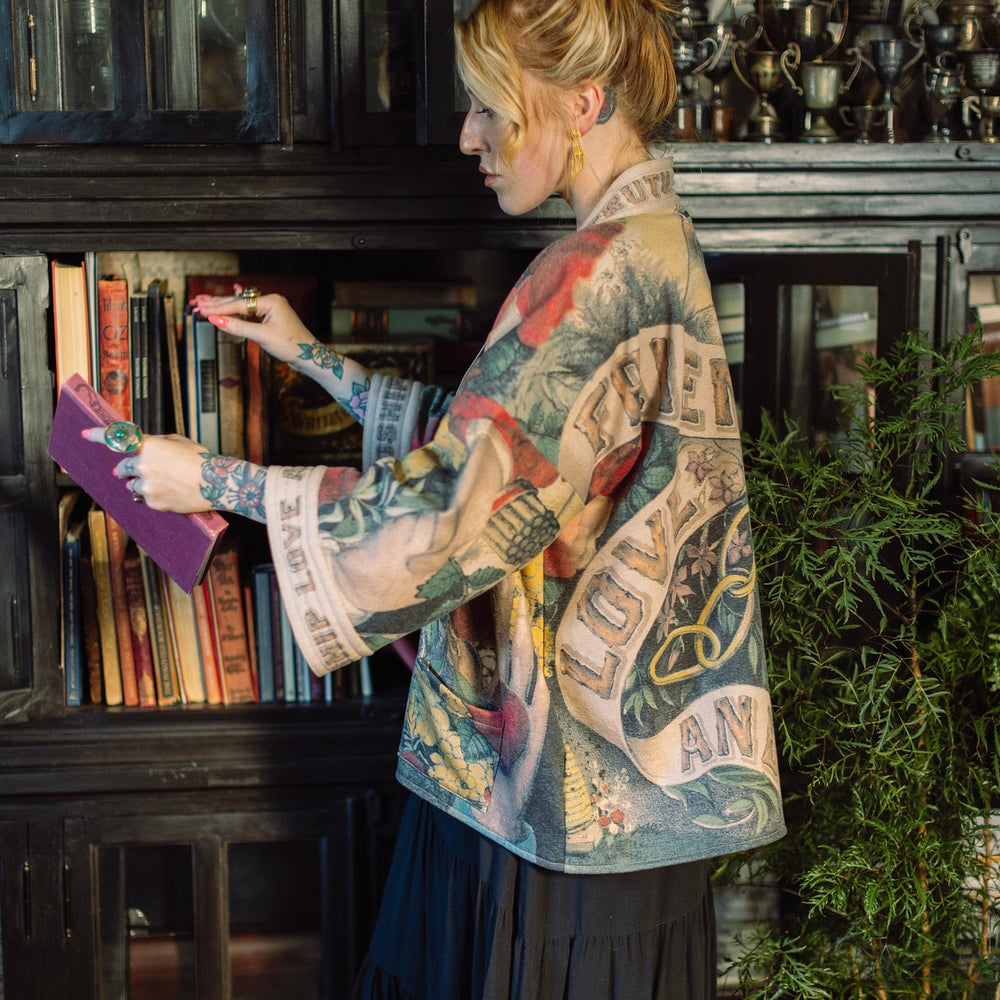 
                  
                    Model wearing cozy printed cardigan with vintage symbols of love, truth, and friendship, featuring charming wood-grain trim and patch pockets – Market of Stars.
                  
                