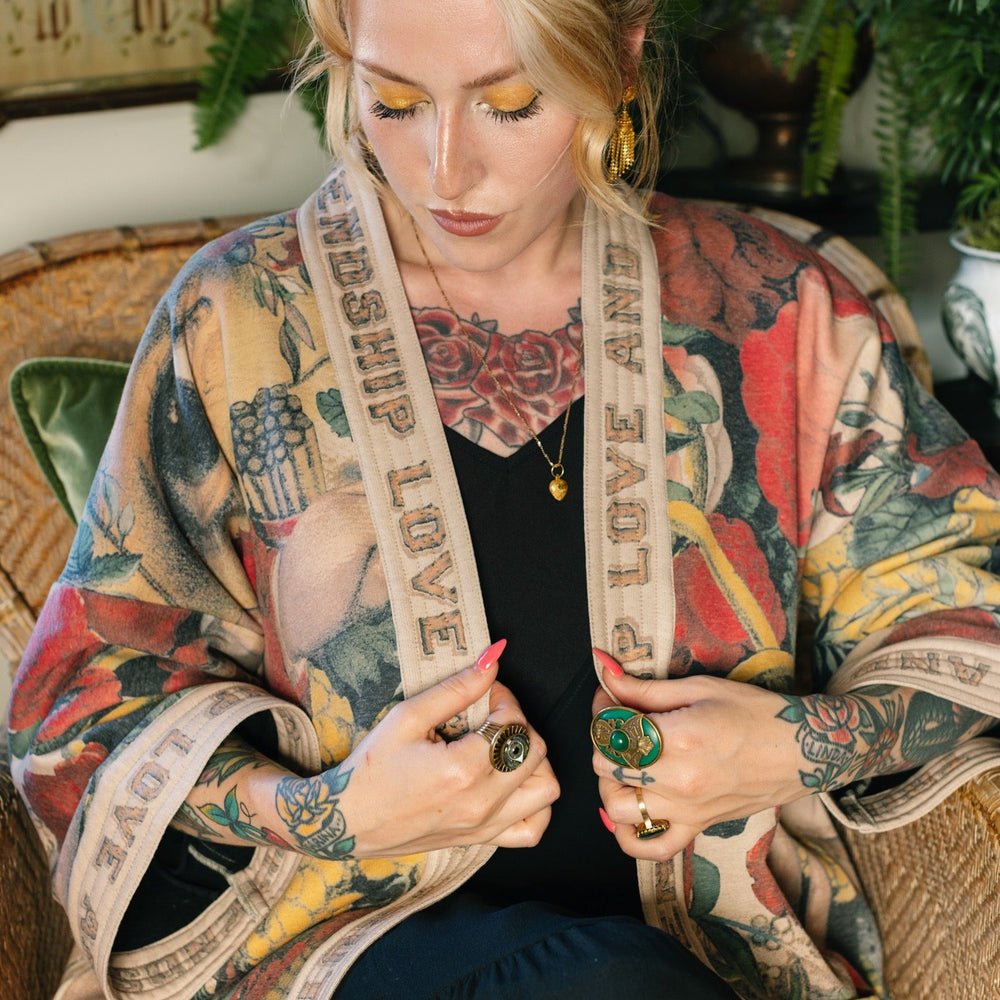 
                  
                    Model wearing cozy printed cardigan with vintage symbols of love, truth, and friendship, featuring charming wood-grain trim and patch pockets – Market of Stars.
                  
                