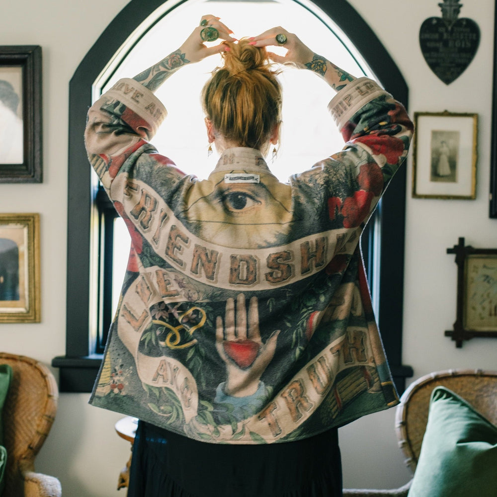 
                  
                    Model wearing cozy printed cardigan with vintage symbols of love, truth, and friendship, featuring charming wood-grain trim and patch pockets – Market of Stars.
                  
                