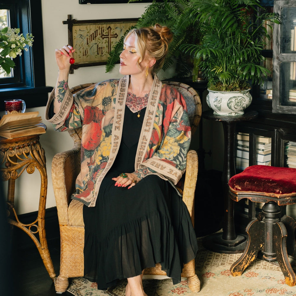 
                  
                    Model wearing cozy printed cardigan with vintage symbols of love, truth, and friendship, featuring charming wood-grain trim and patch pockets – Market of Stars.
                  
                
