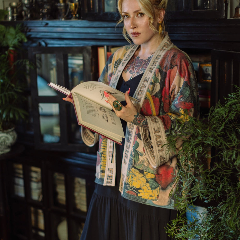 
                  
                    Model wearing cozy printed cardigan with vintage symbols of love, truth, and friendship, featuring charming wood-grain trim and patch pockets – Market of Stars.
                  
                