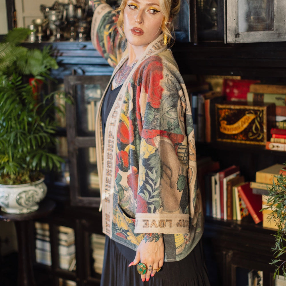 
                  
                    Model wearing cozy printed cardigan with vintage symbols of love, truth, and friendship, featuring charming wood-grain trim and patch pockets – Market of Stars.
                  
                