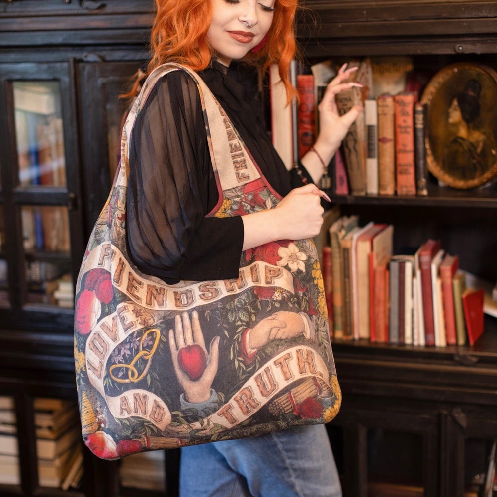 
                  
                    Model holding Friendship Love and Truth tote featuring historic symbols of cooperation, teamwork, eternal love, and truth from an 1880s print – Market of Stars.
                  
                