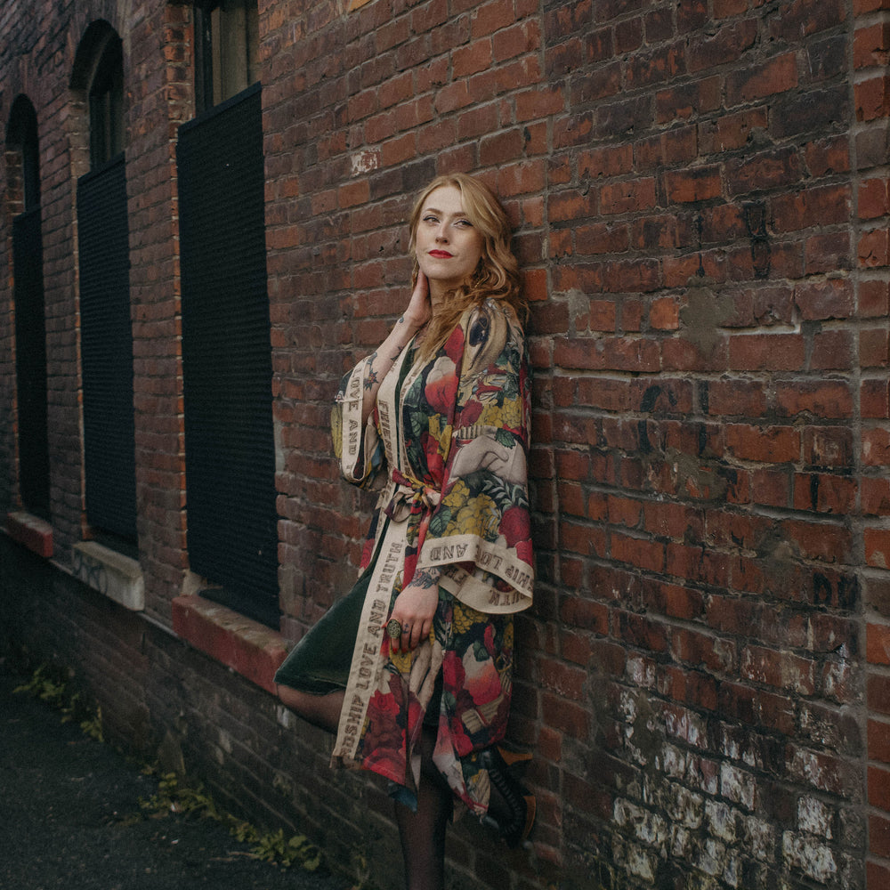 
                  
                    Model wearing our long, eclectic opera duster featuring vintage symbols of love, kindness, and truth in a bold archive-inspired print with removable belt – Market of Stars.
                  
                
