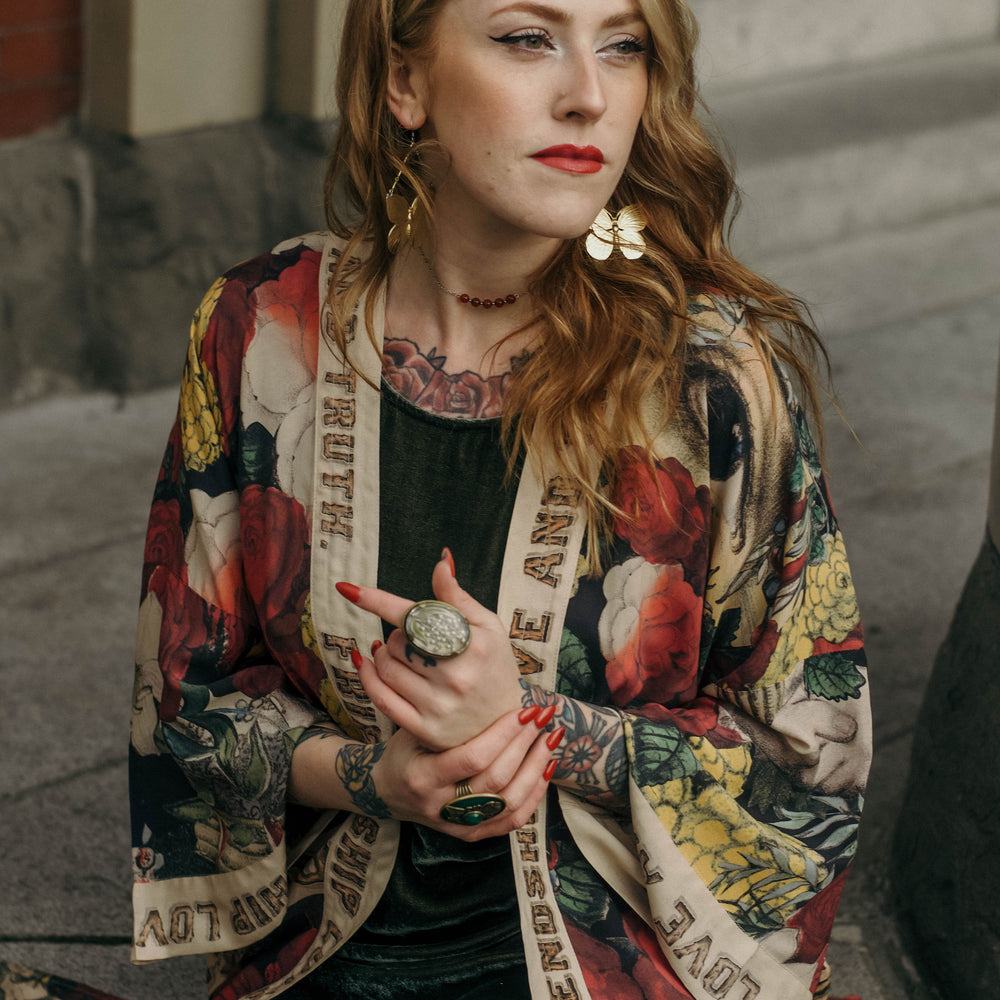 
                  
                    Model wearing our long, eclectic opera duster featuring vintage symbols of love, kindness, and truth in a bold archive-inspired print with removable belt – Market of Stars.
                  
                