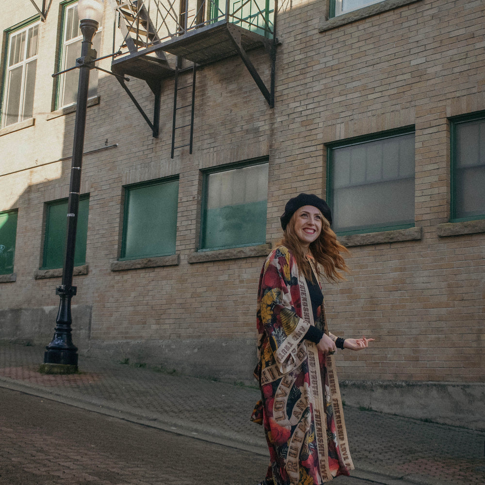 
                  
                    Model wearing our long, eclectic opera duster featuring vintage symbols of love, kindness, and truth in a bold archive-inspired print with removable belt – Market of Stars.
                  
                