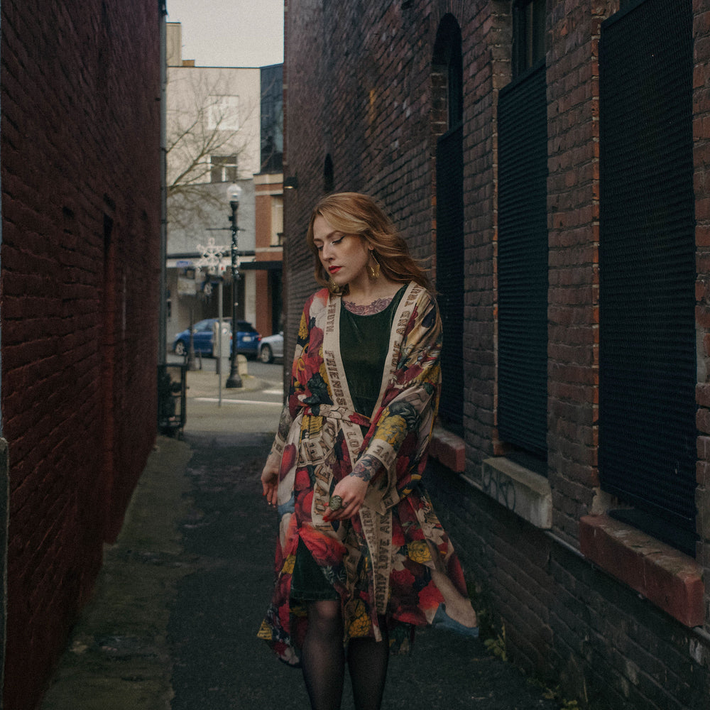 
                  
                    Model wearing our long, eclectic opera duster featuring vintage symbols of love, kindness, and truth in a bold archive-inspired print with removable belt – Market of Stars.
                  
                
