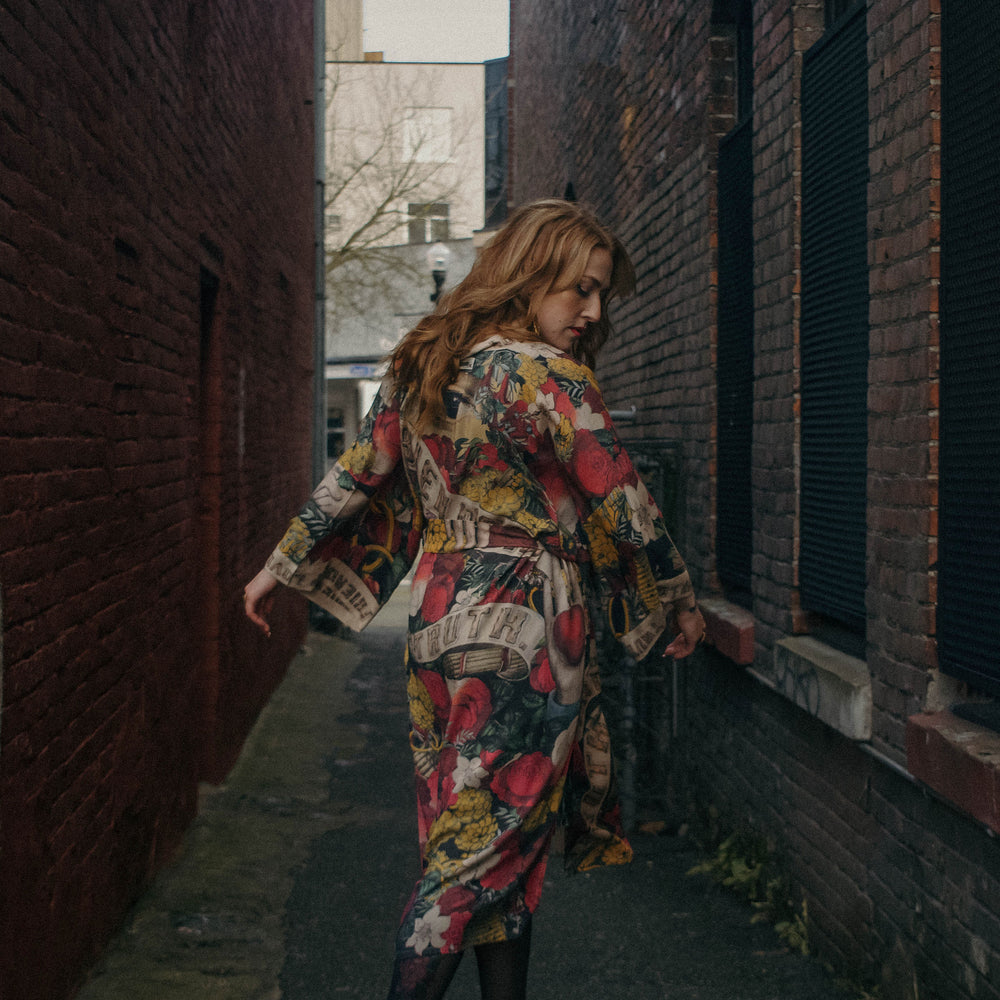 
                  
                    Model wearing our long, eclectic opera duster featuring vintage symbols of love, kindness, and truth in a bold archive-inspired print with removable belt – Market of Stars.
                  
                