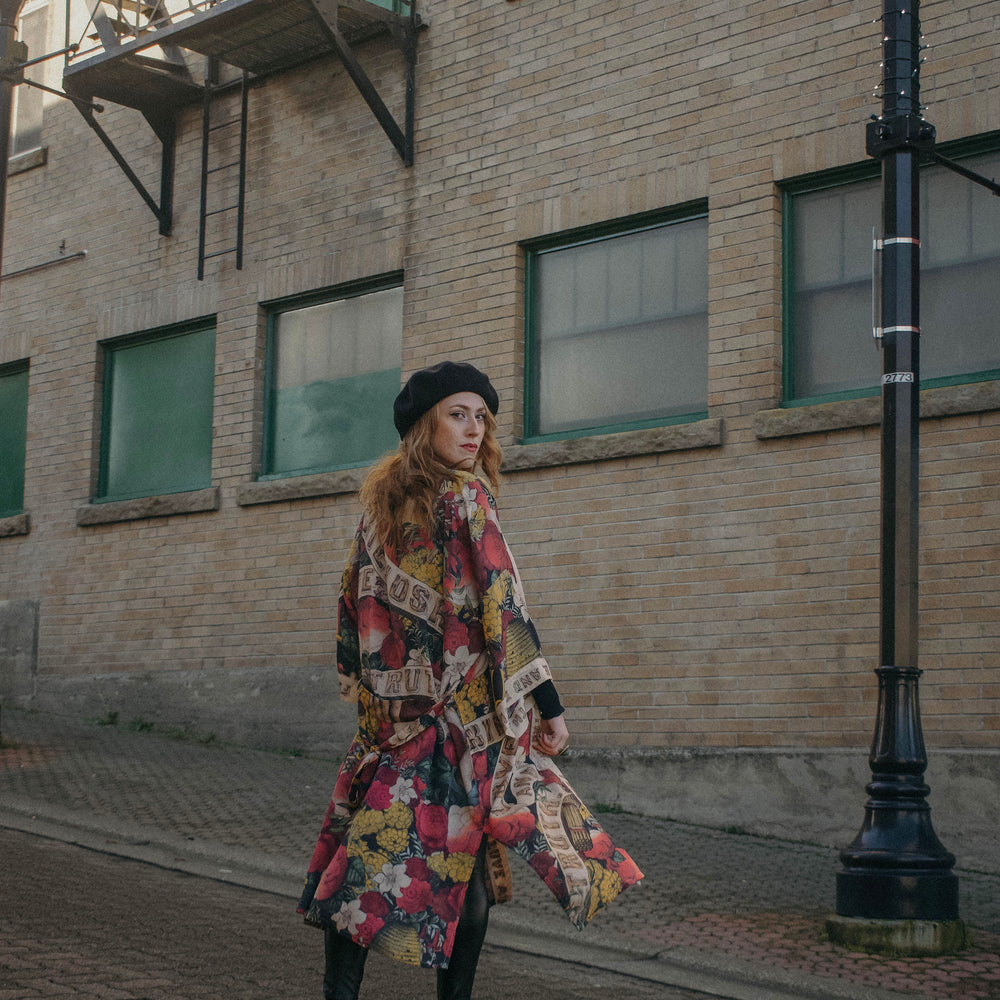 
                  
                    Model wearing our long, eclectic opera duster featuring vintage symbols of love, kindness, and truth in a bold archive-inspired print with removable belt – Market of Stars.
                  
                