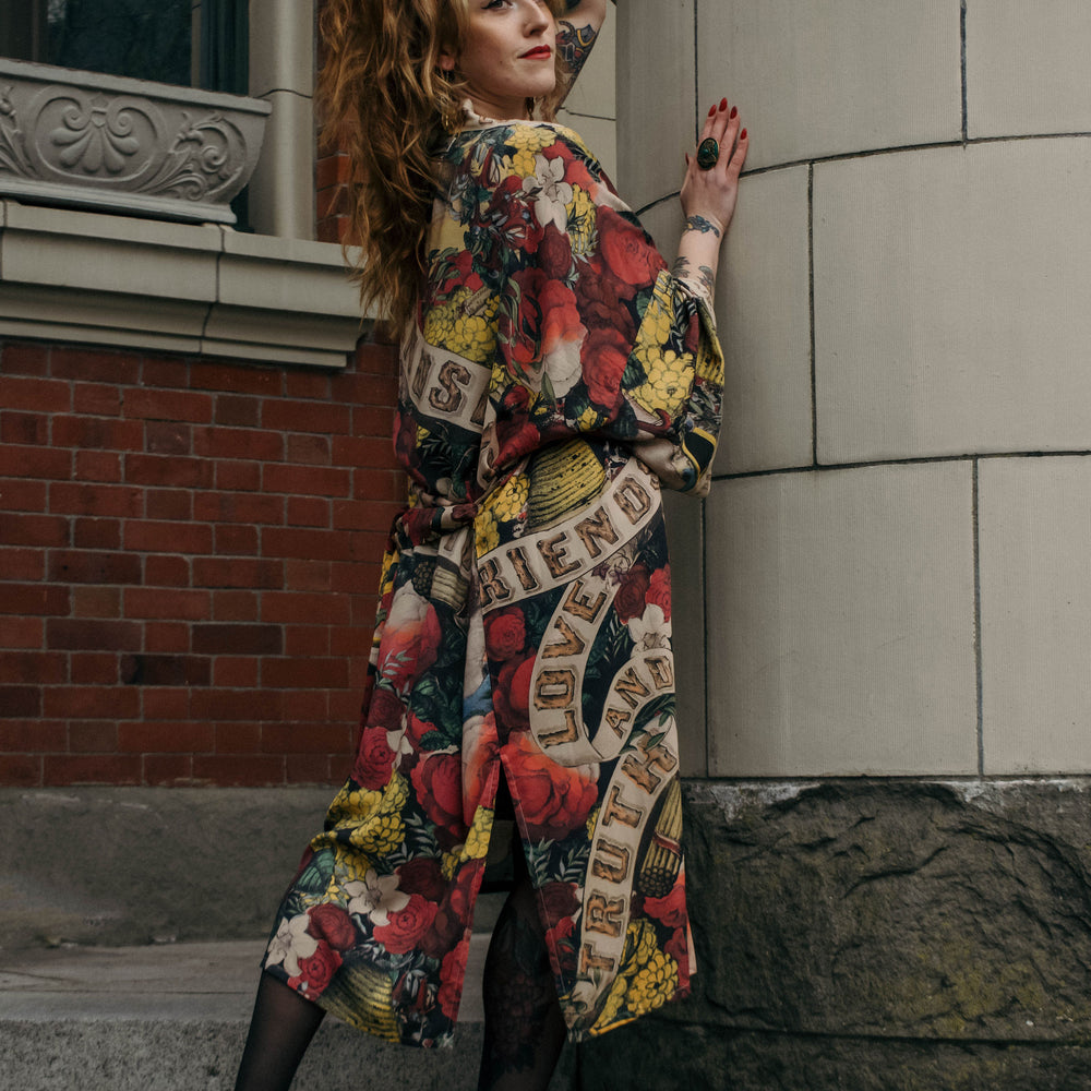 
                  
                    Model wearing our long, eclectic opera duster featuring vintage symbols of love, kindness, and truth in a bold archive-inspired print with removable belt – Market of Stars.
                  
                