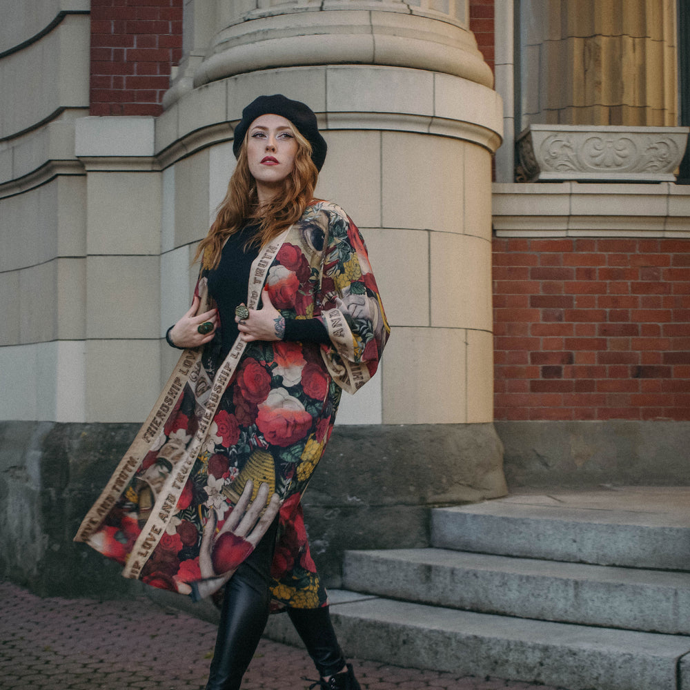 
                  
                    Model wearing our long, eclectic opera duster featuring vintage symbols of love, kindness, and truth in a bold archive-inspired print with removable belt – Market of Stars.
                  
                
