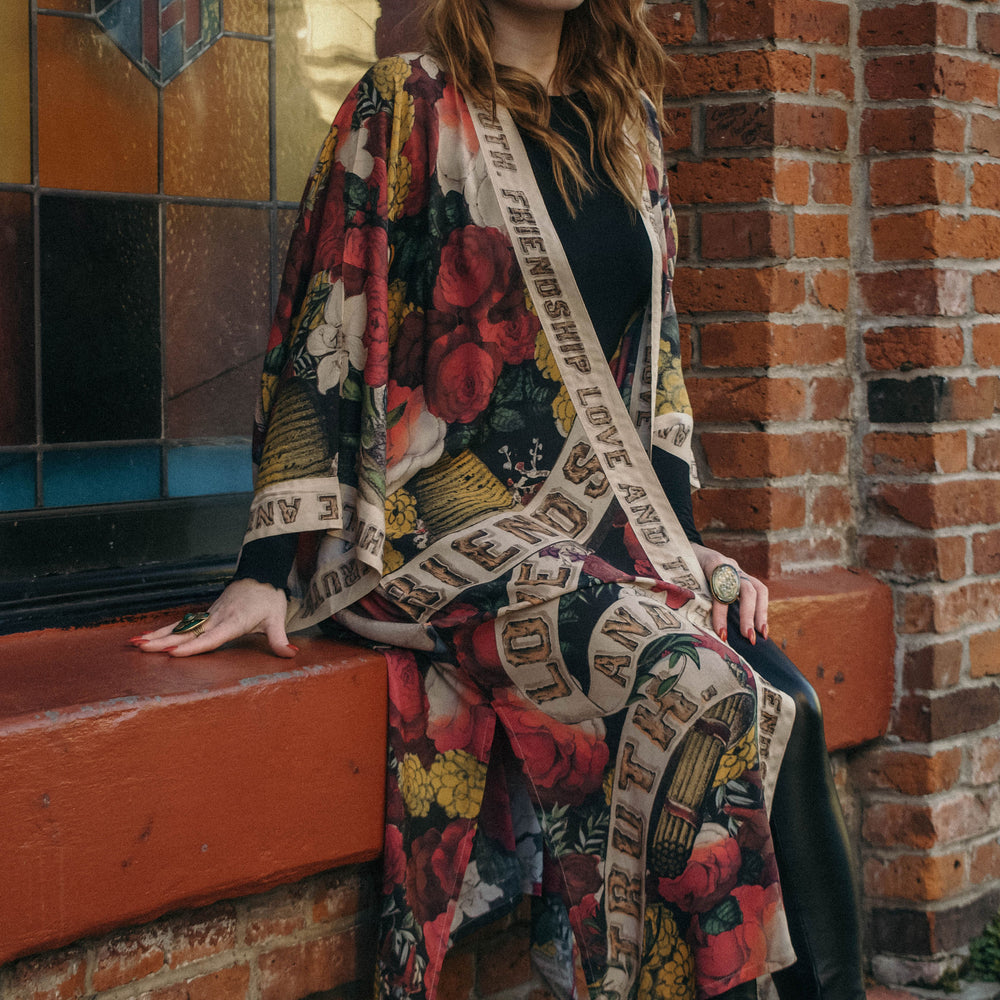 
                  
                    Model wearing our long, eclectic opera duster featuring vintage symbols of love, kindness, and truth in a bold archive-inspired print with removable belt – Market of Stars.
                  
                