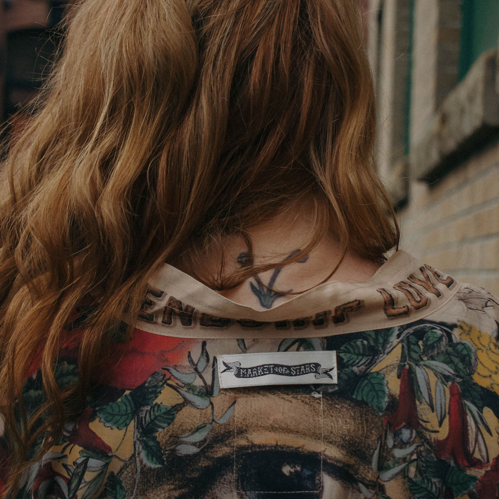 
                  
                    Model wearing our long, eclectic opera duster featuring vintage symbols of love, kindness, and truth in a bold archive-inspired print with removable belt – Market of Stars.
                  
                