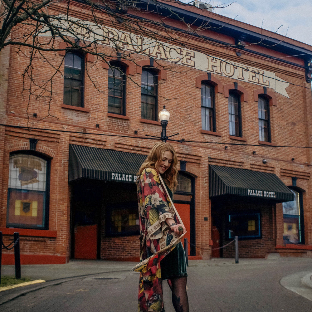 
                  
                    Model wearing our long, eclectic opera duster featuring vintage symbols of love, kindness, and truth in a bold archive-inspired print with removable belt – Market of Stars.
                  
                