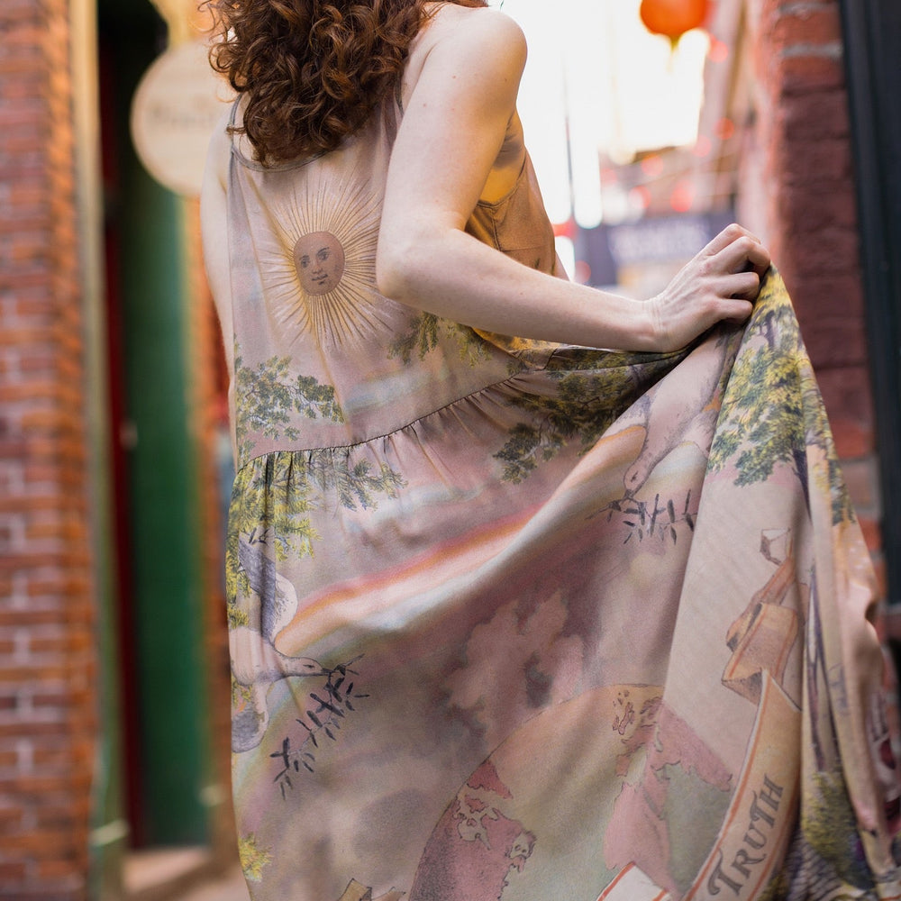 
                  
                    Model wearing sun-washed Bohéme slip dress featuring historic symbols of friendship, love, and truth in soft lavender, sage, gold, and aqua – Market of Stars.
                  
                