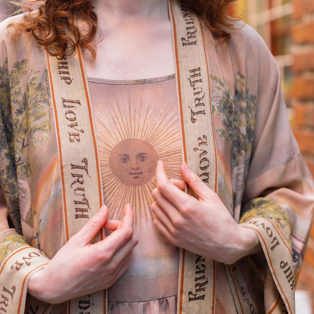
                  
                    Model wearing sun-washed Bohéme slip dress featuring historic symbols of friendship, love, and truth in soft lavender, sage, gold, and aqua – Market of Stars.
                  
                