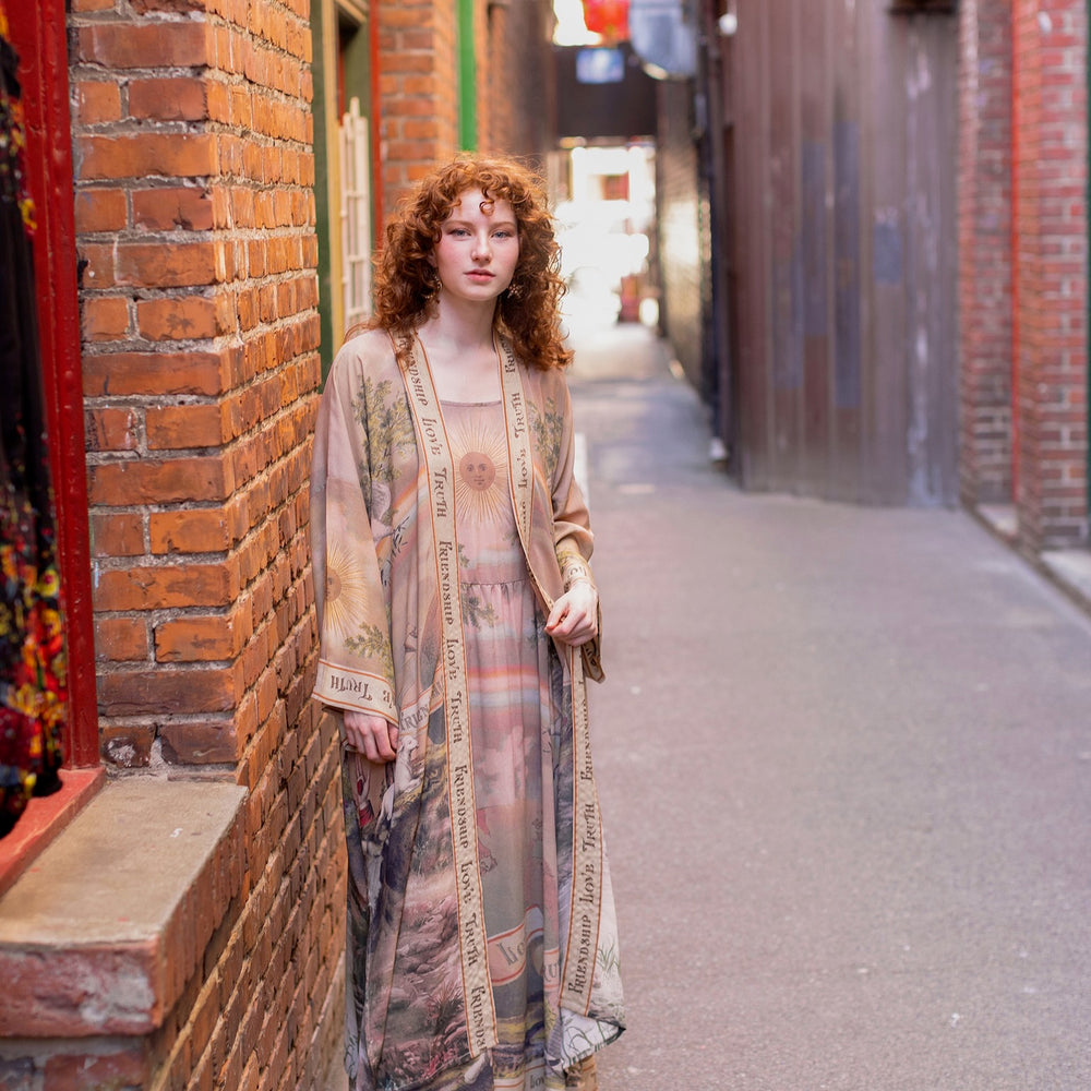 
                  
                    Model wearing sun-washed Bohéme slip dress featuring historic symbols of friendship, love, and truth in soft lavender, sage, gold, and aqua – Market of Stars.
                  
                