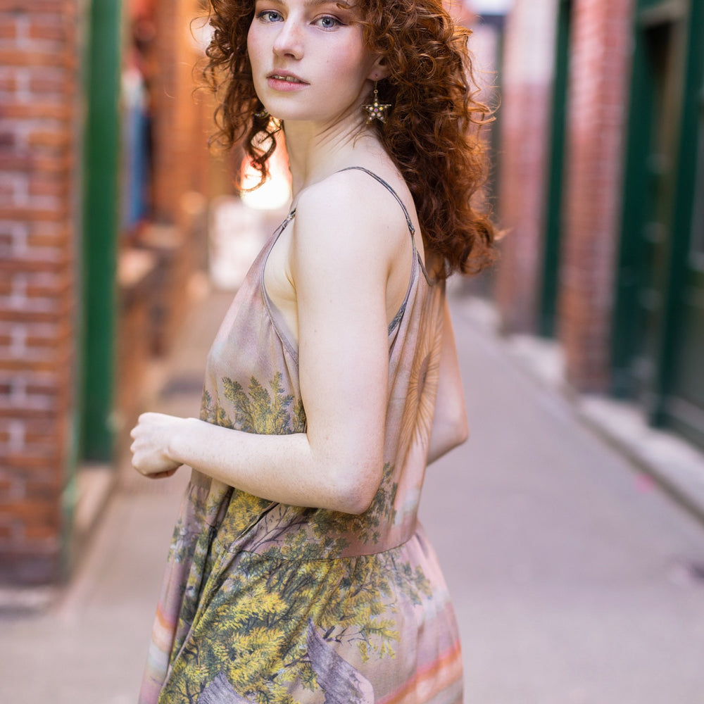 
                  
                    Model wearing sun-washed Bohéme slip dress featuring historic symbols of friendship, love, and truth in soft lavender, sage, gold, and aqua – Market of Stars.
                  
                