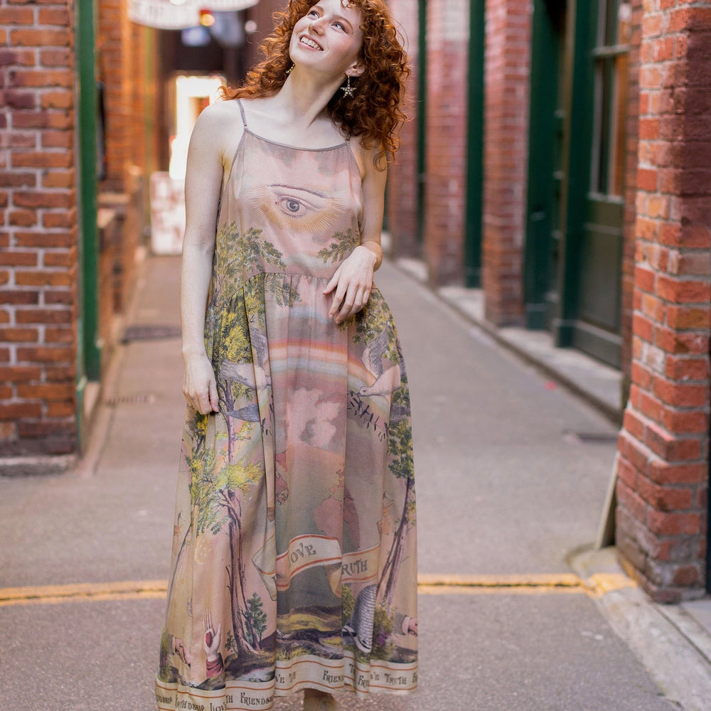
                  
                    Model wearing sun-washed Bohéme slip dress featuring historic symbols of friendship, love, and truth in soft lavender, sage, gold, and aqua – Market of Stars.
                  
                